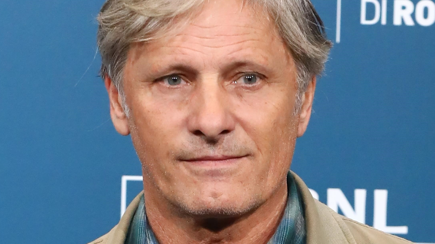 Viggo Mortensen. Mężczyzna z jasnymi włosami, w szarej kurtce, patrzy prosto w obiektyw.