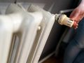 Osoba regulująca temperaturę na kaloryferze za pomocą pokrętła. Widziana część ręki i kaloryfer.
