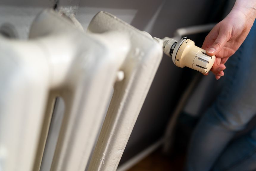 Osoba regulująca temperaturę na kaloryferze za pomocą pokrętła. Widziana część ręki i kaloryfer.