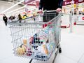 Koszyk zakupowy pełen artykułów spożywczych w supermarkecie. W tle klienci przy kasach.