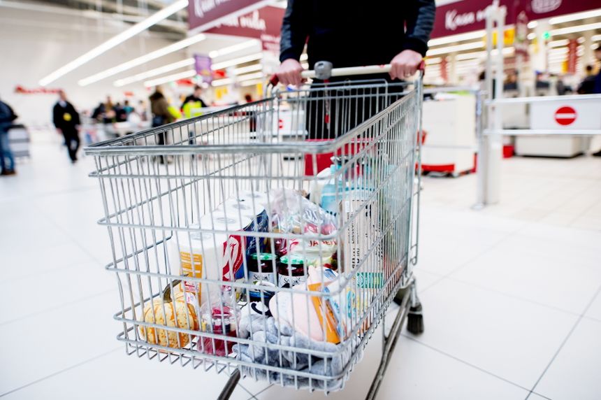 Koszyk zakupowy pełen artykułów spożywczych w supermarkecie. W tle klienci przy kasach.