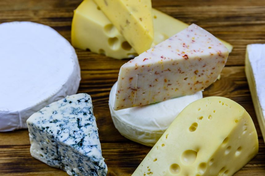 Różnorodne sery na drewnianym tle: Brie, blue cheese, Gouda i sery z przyprawami.