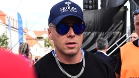 Skolim w czapce z daszkiem, okularach słonecznych i srebrnym łańcuchem, tłum w tle.