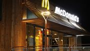 Wizytówka McDonald's, drewniana elewacja, podświetlona, nocą z logo w żółtym i białym.