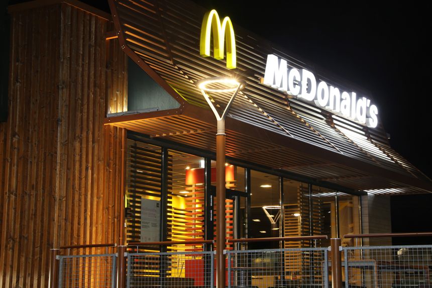 Wizytówka McDonald's, drewniana elewacja, podświetlona, nocą z logo w żółtym i białym.