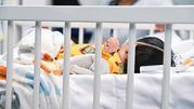 Dziecko w szpitalnym łóżku, owinięte w koc, z widoczną ręką i monitorującym sprzętem.