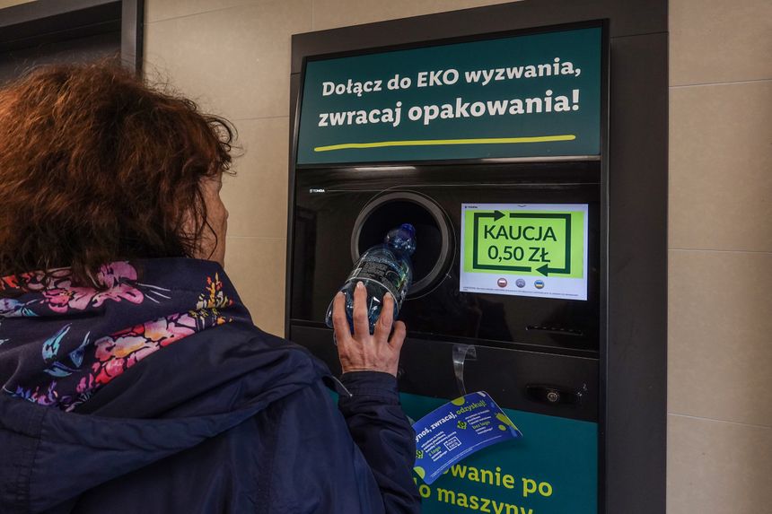 Kobieta wrzuca butelkę do maszyny zwrotnej z napisem o zwrocie kaucji 0,50 zł.