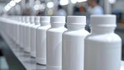 Zdjęcie przedstawia rząd białych butelek na taśmie produkcyjnej w fabryce.