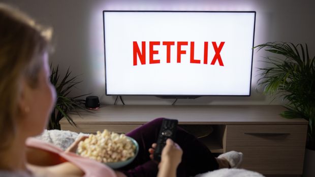 Kobieta z popcornem ogląda Netflix na telewizorze w domowym wnętrzu.