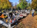 Cmentarz w jesiennych liściach, zapalone znicze i kwiaty na nekropoliach, osoba spacerująca.