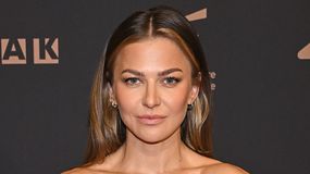 Anna Lewandowska z długimi włosami, uśmiechająca się na tle ciemnej ścianki z logo wydarzenia.