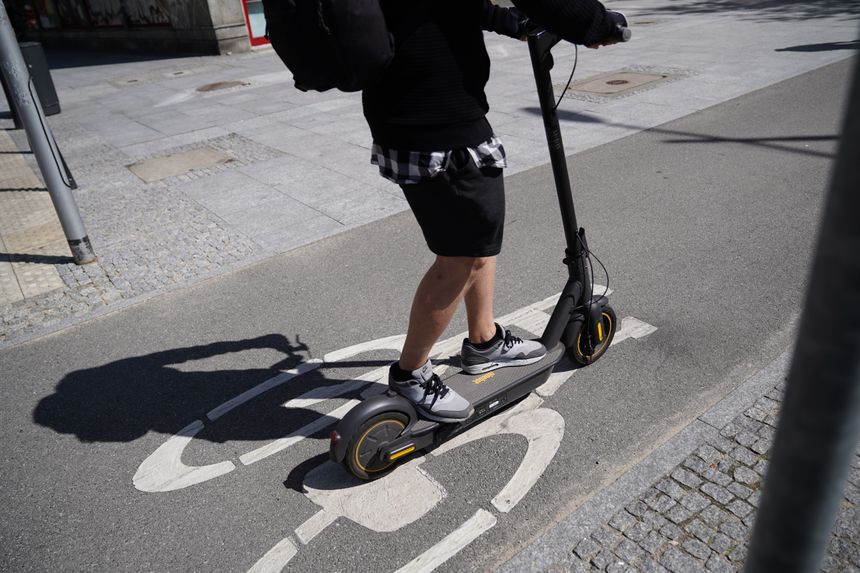 Mężczyzna na hulajnodze elektrycznej porusza się po ścieżce rowerowej w mieście.