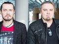 Para mężczyzn w eleganckich ubraniach, stojących blisko siebie w jasnym wnętrzu.