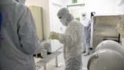 Grupa osób w białych fartuchach ochronnych w laboratorium. W tle sprzęt laboratoryjny.