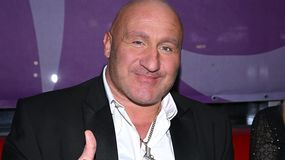 Marcin Najman w garniturze uśmiechający się i pokazujący 