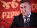 Cezary Kulesza w garniturze z niebieską krawatem, siedzący przy stole z logo PZPN w tle.