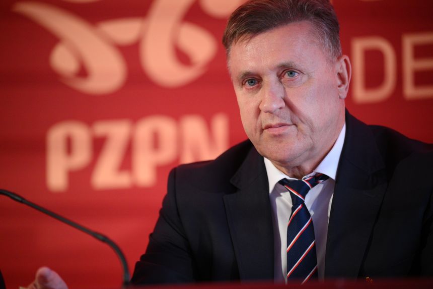 Cezary Kulesza w garniturze z niebieską krawatem, siedzący przy stole z logo PZPN w tle.
