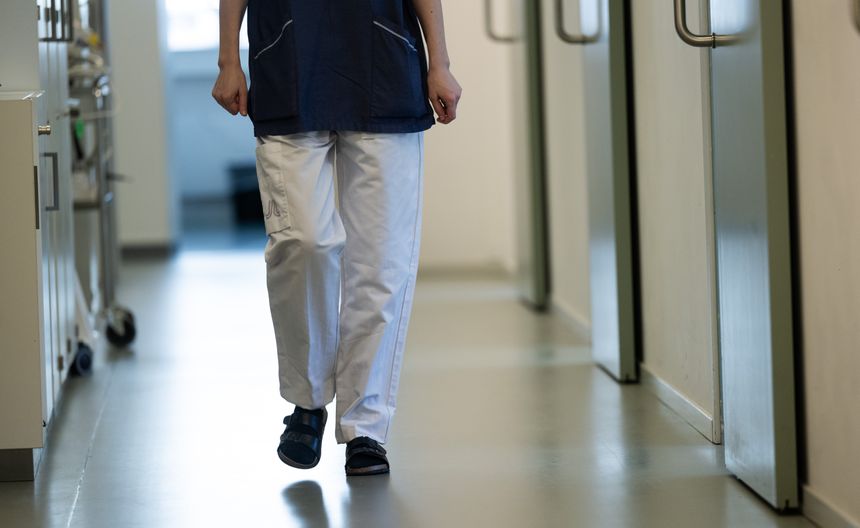 Na zdjęciu widoczna jest osoba w uniformie medycznym idąca korytarzem szpitalnym.
