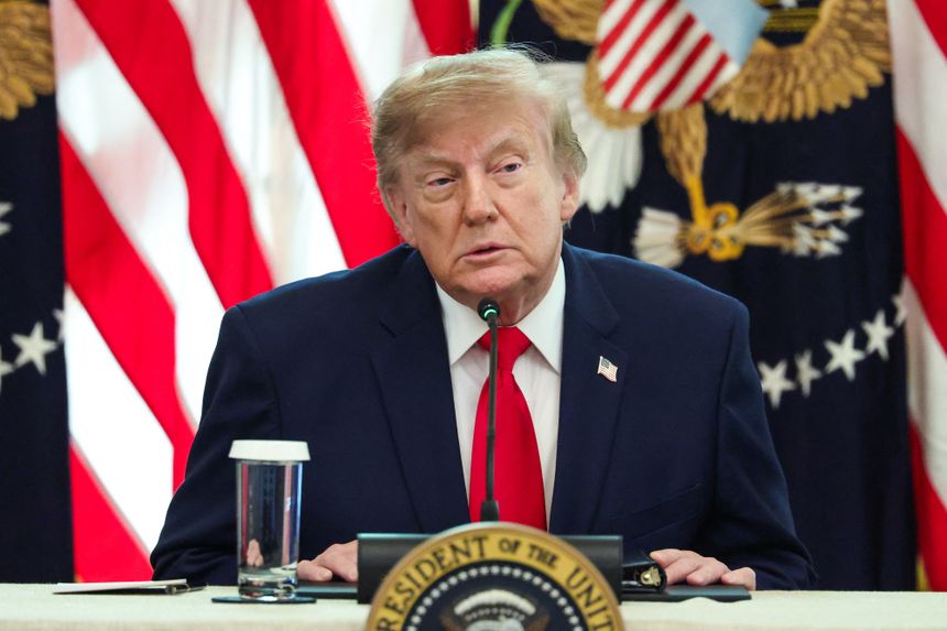 Na zdjęciu mężczyzna w garniturze siedzi przy stole, za nim flagi USA i godło.