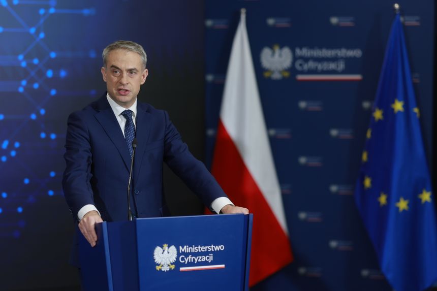 Mężczyzna w garniturze przemawia przy mównicy Ministerstwa Cyfryzacji, w tle flagi Polski i UE.