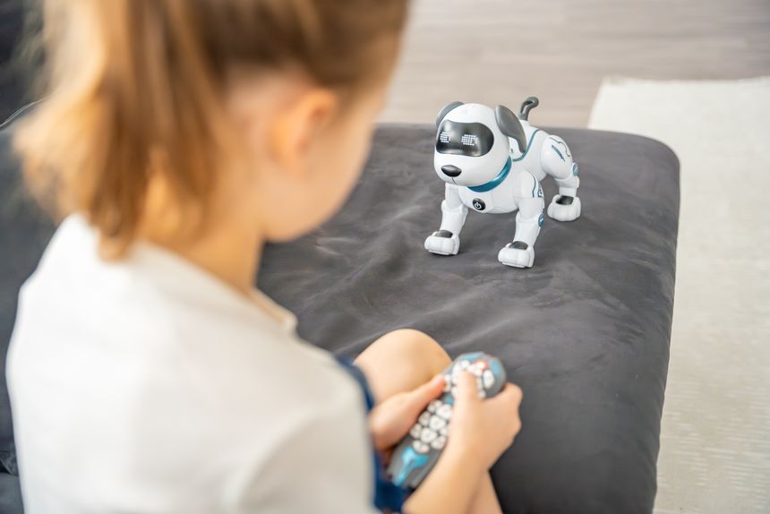Dziewczynka siedzi na kanapie z pilotem w ręku, patrząc na robota-psa.