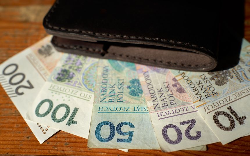 Portfel stojący na stole z polskimi banknotami: 20, 50, 100 i 200 złotych.