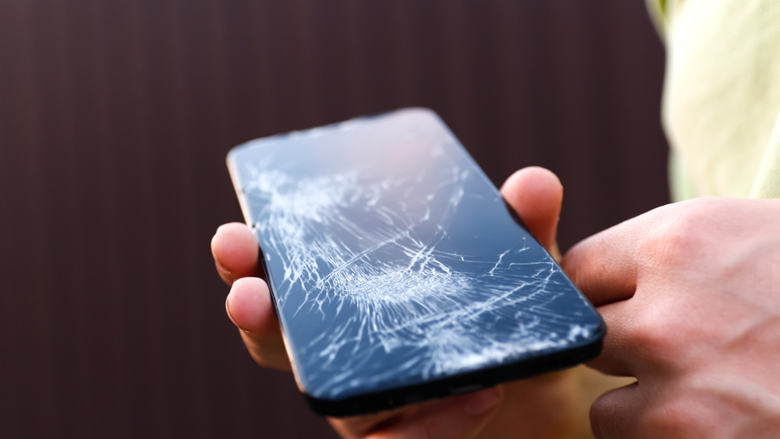 Zniszczony telefon komórkowy trzymany w dłoni, pokryty pęknięciami na ekranie.