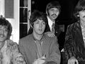 Czterech mężczyzn w stylowych ubraniach, siedzących w pomieszczeniu. To znany zespół The Beatles.