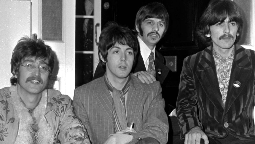 Czterech mężczyzn w stylowych ubraniach, siedzących w pomieszczeniu. To znany zespół The Beatles.
