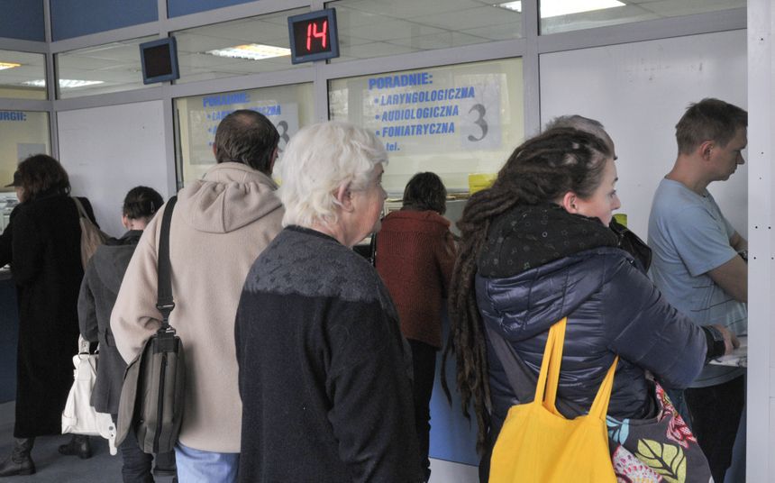 Osoby czekające w kolejce w przychodni, widać numery i gabinety poradni.