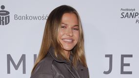 Na zdjęciu Anna Lewandowska z długimi włosami, uśmiechnięta, w szarej kurtce, na tle z napisami.