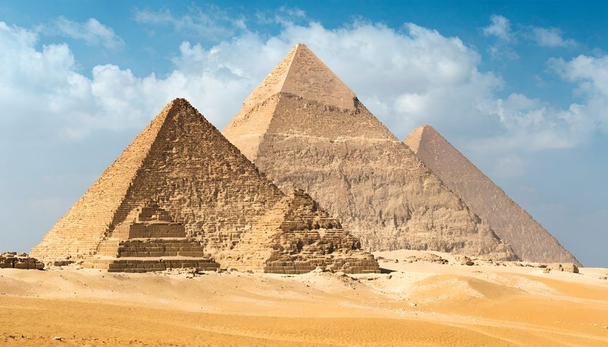 Trzy wielkie piramidy w Egipcie, otoczone piaskiem, pod błękitnym niebem z chmurami.