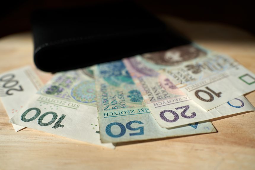 Zestaw polskich banknotów o nominałach 20 zł, 50 zł, 100 zł i 200 zł na tle portfela.