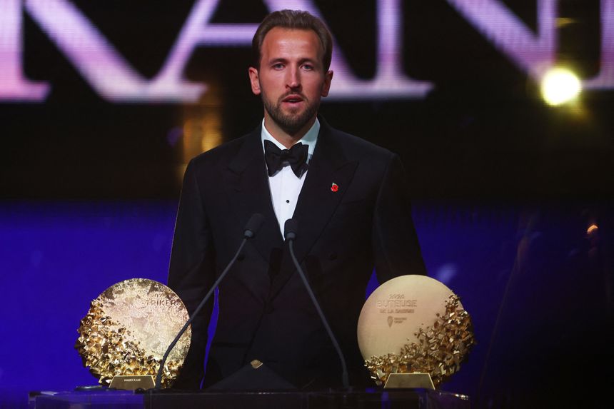 Harry Kanee mówi z podium, obok niego dwa złote trofea.