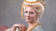 Kobieta z blond włosami w kok, uśmiechająca się, w stylowej sukience z ozdobami.