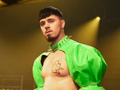 Model w jaskrawo zielonej kurtce, z gołą klatką piersiową i w ostrym obroży, na scenie.