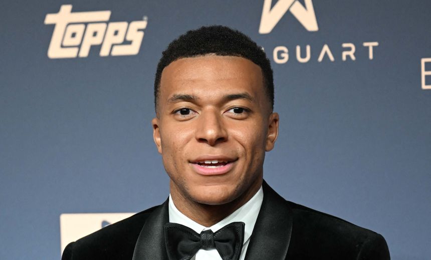 Kylian Mbappe w eleganckim garniturze z czarną muszką na tle ciemnego tła.