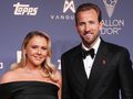 Harry Kane z żoną w eleganckich strojach na niebieskim tle.