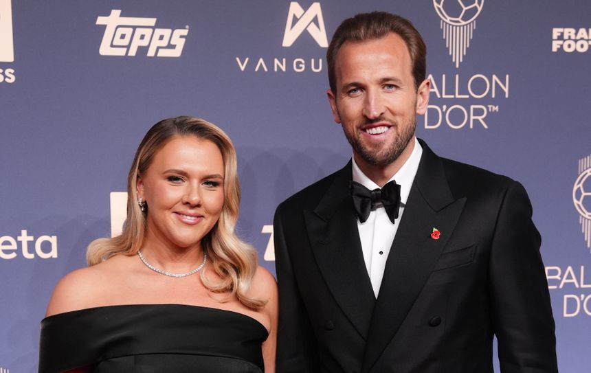 Harry Kane z żoną w eleganckich strojach na niebieskim tle.