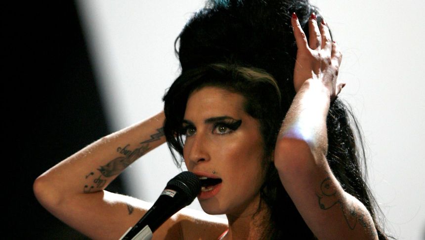 Na zdjęciu artystka śpiewająca do mikrofonu, z dużymi, ciemnymi włosami i mocnym makijażem.
