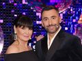 Rafał Maserak i Iwona Pavlović uśmiechają się na tle świecących dekoracji. Oboje są elegancko ubrani.