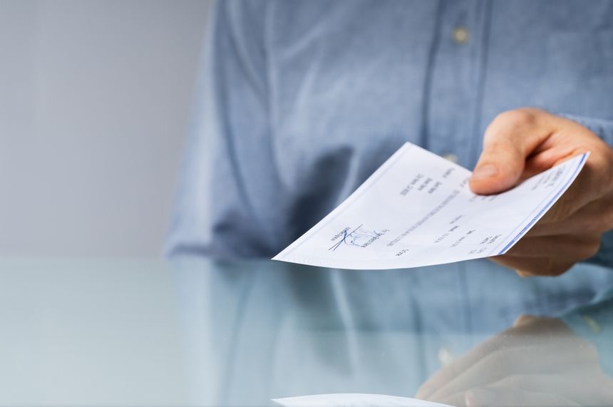 Mężczyzna podaje dokument, leżący na szklanym stole, w tle jasna ściana.