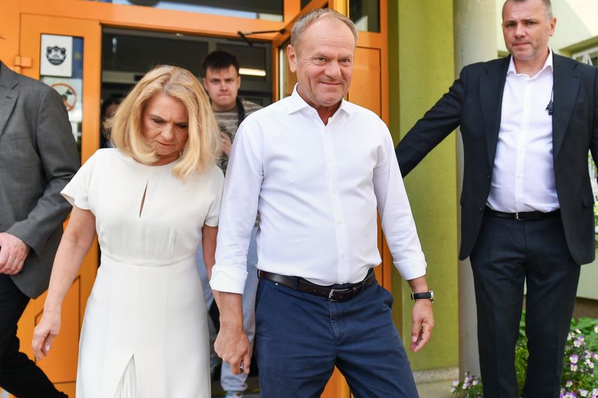 Dwoje ludzi wychodzi z budynku. Mężczyzna w białej koszuli, kobieta w białej sukience.