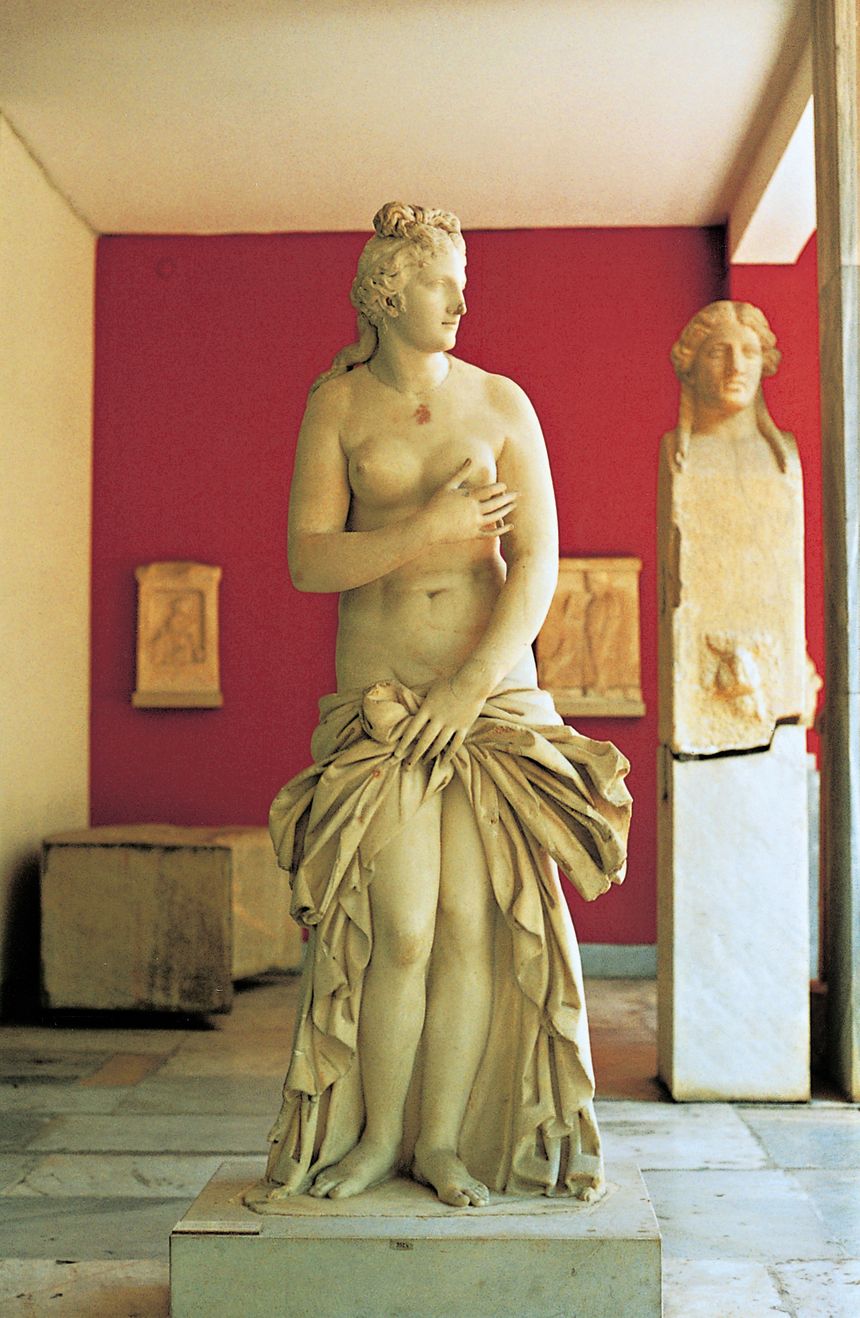 Starożytna rzeźba Afrodyty z odkrytym ciałem, ustawiona na jasnym tle w muzeum.