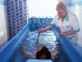 Woda w niebieskiej wannie, terapeuta obsługujący urządzenie. Osoba w wodzie relaksuje się.