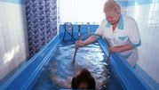 Woda w niebieskiej wannie, terapeuta obsługujący urządzenie. Osoba w wodzie relaksuje się.