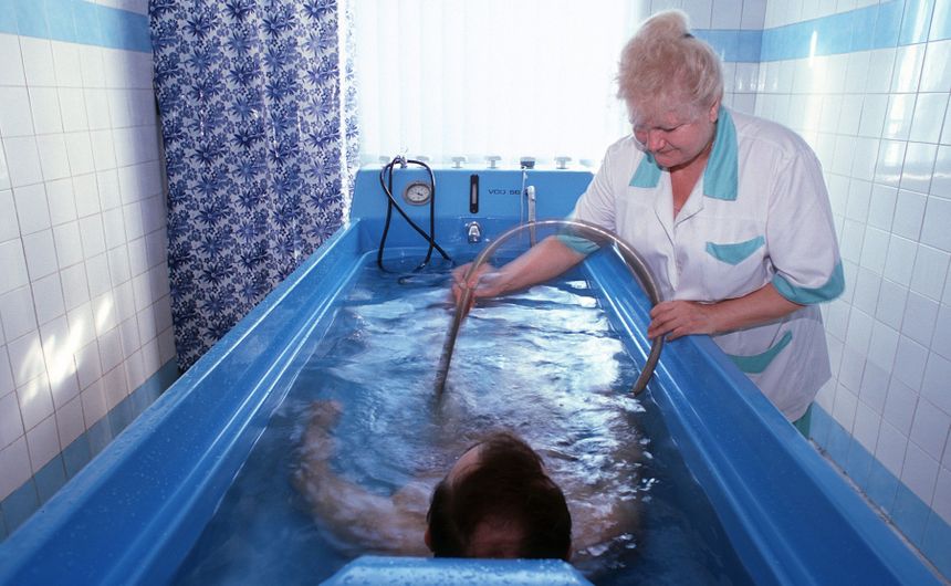 Woda w niebieskiej wannie, terapeuta obsługujący urządzenie. Osoba w wodzie relaksuje się.